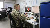 Ein Soldat sitzt im Büro am Schreibtisch und schaut konzentriert auf einen der beiden Bildschirme