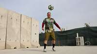 Ein Soldat in Sportkleidung kickt einen Ball in die Luft. Im Hintergrund befindet sich eine große Betonwand