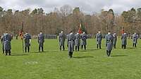 Auf einem Rasen stehen Soldaten mit Fahnen in einer angetretenen Formation.
