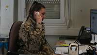 Eine Soldatin sitzt an einem Schreibtisch mit PC und telefoniert
