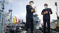 Zwei Marineoffiziere in dunkelblauer Uniform stehen auf dem Oberdeck eines Schiffs und führen ein Gespräch.