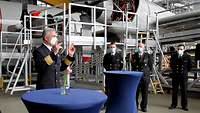 Vier Marinesoldaten in dunkelblauer Uniform stehen in einer Halle. Im Hintergrund ein viermotoriges Propellerflugzeug.