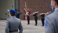 Blechblasmusiker spielen; im Vordergrund zwei Soldaten in Dienstanzug und mit blauem Barrett.