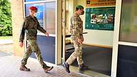 Ein deutscher und ein britischer Soldat mit Mund-Nasenschutz betreten ein Gebäude mit verglastem Eingangsbereich.