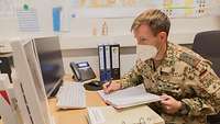 Ein Soldat schreibt Notizen in ein Buch während er auf einen Computer Bildschirm schaut.