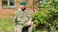 Ein Soldat in Uniform kniet auf einer Wiese vor einem Gebäude. 