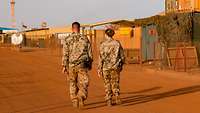 Ein Soldat und eine Soldatin laufen auf einer Straße in einem Camp