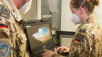 Eine Soldatin arbeitet am Laptop, ein Soldat schaut zu. Beide tragen einen Mund-Nasen-Schutz
