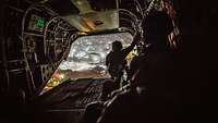 Soldaten schauen bei Nacht aus dem offenen Heck während eines Fluges mit dem Transporthubschrauber CH-47