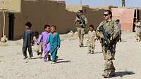 Mehrere Kinder begleiten zwei Soldaten bei ihrer Patroullie durch eine Ortschaft