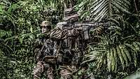 Zwei Kommandosoldaten laufen mit dem Gewehr im Anschlag durch den grünen Dschungel.