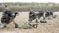 Mehrere Soldaten knien in einer Reihe mit Gewehren im Anschlag auf dem Truppenübungsplatz