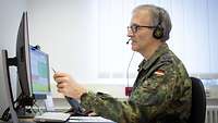 A soldier sits in front of his PC, pointing with a pen on his screen while explaining something.