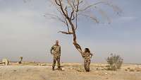 Eine Soldatin und ein Soldat stehen vor einem ausgetrockneten Baum in der jordanischen Wüste 