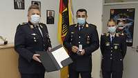 Zwei Soldaten und eine Soldaten stehen mit Masken zusammen bei der Verleihung des Ehrenkreuzes.