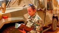 Eine Soldatin steht neben einem militärischen Auto und hält einen Ordner in der Hand, in dem sie liest