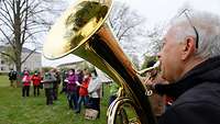 Ein Tuba-Bläser musiziert auf einer Wiese in der Kaserne, im Hintergrund Wallfahrer bei der Andacht