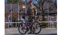 Major Daniel Calthorpe standing at the Bundeswehr Command and Staff College’s entrance with his bicycle