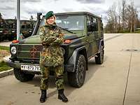 A blonde female soldier in front of a green cross-country vehicle