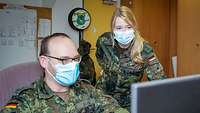 A blonde female soldier and a male soldier discussing something in front of a computer