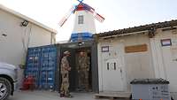 Zwei Soldaten stehen vor Containern, im Hintergrund steht eine Windmühle in den Farben der niederländischen Flagge