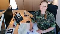 A servicewoman is sitting at a desk and is smiling at the camera