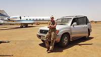 A servicewoman leaning against a car, with an aircraft in the background