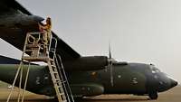 A servicewoman is standing on a ladder and working on an aircraft engine