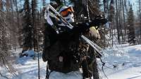 Ein Soldat steht mit seinem Gewehr im Anschlag in einem verschneiten Wald.