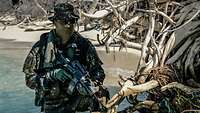 Ein Soldat in Gefechtsanzug steht mit seinem Gewehr in einem Mangrovenwald.