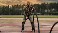 Ein Soldat macht auf einem Sportplatz eine Sportübung mit Seilen.