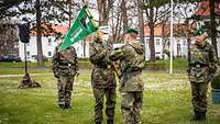 Ein Soldat übergibt einem anderen Soldaten einen grünen Wimpel, zwei Soldaten stehen still.