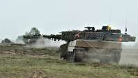 Drei Kampfpanzer Leopard fahren hintereinander über ein grünes Feld.