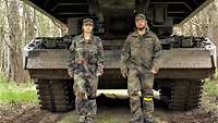 Zwei Pioniere in Uniform stehen draußen vor einem Panzer mit großen Metallaufbauten, die beide überragen.