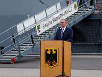 Mann im Jacket steht hinter einem Rednerpult. Im Hintergrund eine Stelling mit dem Schriftzug Fregatte „Sachsen-Anhalt“.