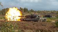 A battle tank fires in the field. A fireball appears at the muzzle of the gun.