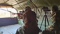 The sniper rifle rests on a rope attached to the cargo area of a truck.