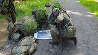 Eine Gruppe von Soldaten schaut auf eine Karte, die vor ihr auf dem Boden liegt. Der Kompass wird zur Orientierung genutzt.