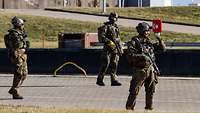 Drei Soldaten in Flecktarnuniform gehen mit großem Abstand über ein gepflastertes Hafenkai.