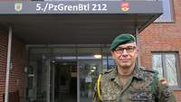 Ein Soldat mit einer goldenen Kordel an seiner rechten Schulter steht vor einem Gebäudeeingang.