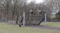 Zwei Soldaten überwinden den höchsten Punkt einer Holzkonstruktion und springen gleich ab.