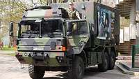 Ein großer Lkw der Bundeswehr in Tarnfarben. Oben an der Fahrertür steht eine Soldatin.