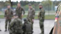 Unscharf im Hintergrund ist eine Gruppe von Soldaten zu sehen. Im Vordergrund das Deutsche Hoheitsabzeichen auf einem Ärmel.