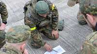 Mehrere Soldaten knien auf dem Boden und stecken die Köpfe über einer Karte zusammen.