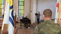 In der Kirche - vordergründig halten Soldaten Flaggen mit Kirchensymbolen, im Hintergrund musizieren und singen andere Soldaten