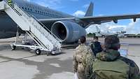 Blick über die Schulter. Drei Soldaten laufen auf einen großen grauen Airbus der Royal Air Force zu.