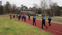 Mehrere Soldaten in blauer Sportbekleidung laufen auf einer roten Tartanbahn eines Sportplatzes.