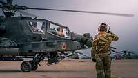 Ein Hubschrauber steht auf der Startbahn, ein Soldat steht daneben und grüßt militärisch.