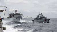 Ein graues Versorgungsschiff und ein graues Kriegsschiff fahren parallel in See.