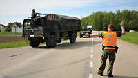 Ein Militärpolizist weist einem Lkw der Bundeswehr den richtigen Weg auf einer Landstraße 